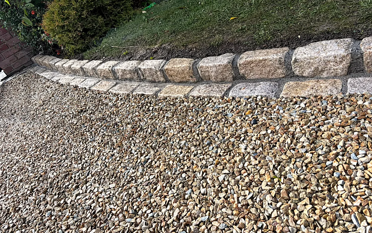 Gravel bedded behind granite cobble edging, with the surface draining away naturally beside the lawn.