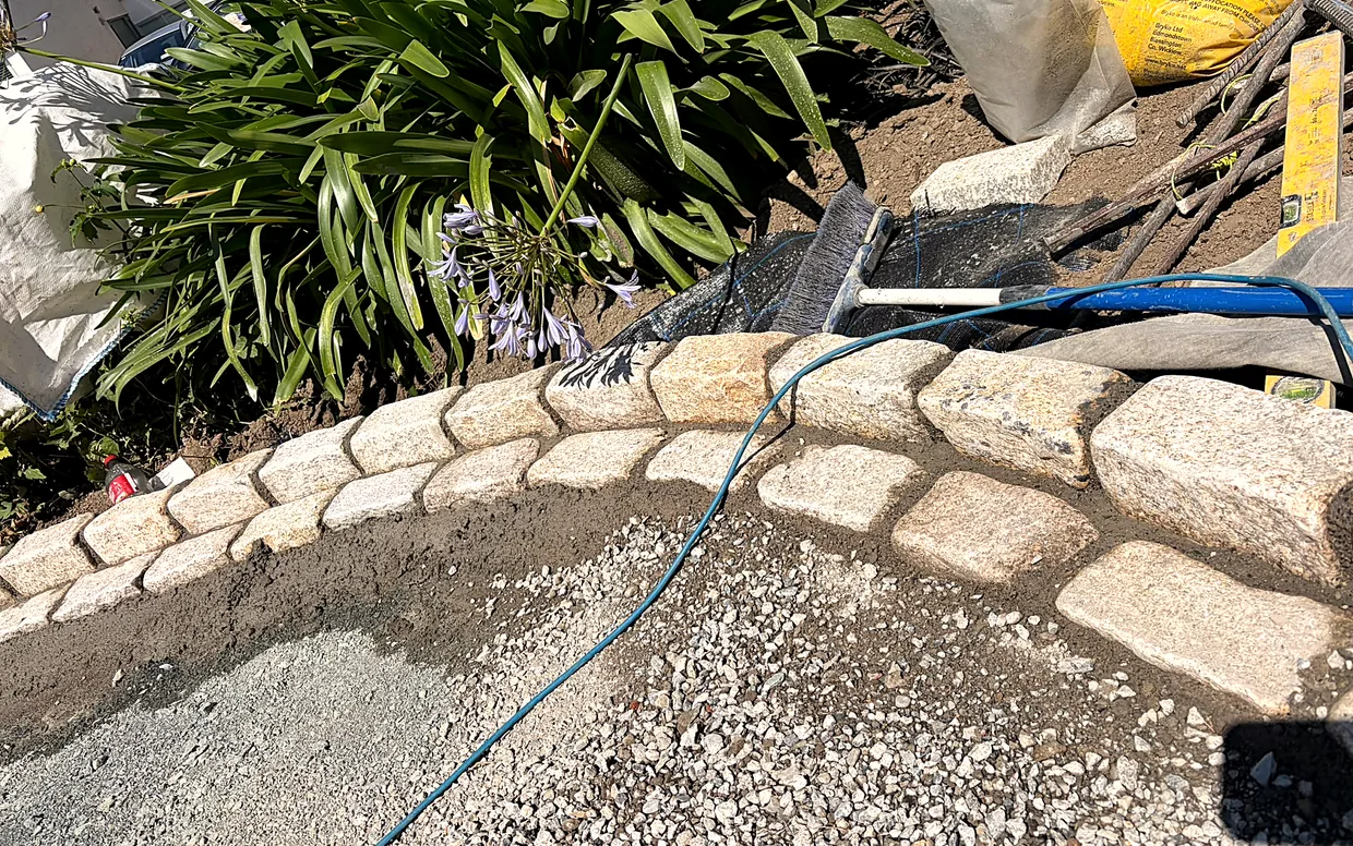 Granite cobble edging set on concrete over a compacted base, before the gravel goes down.