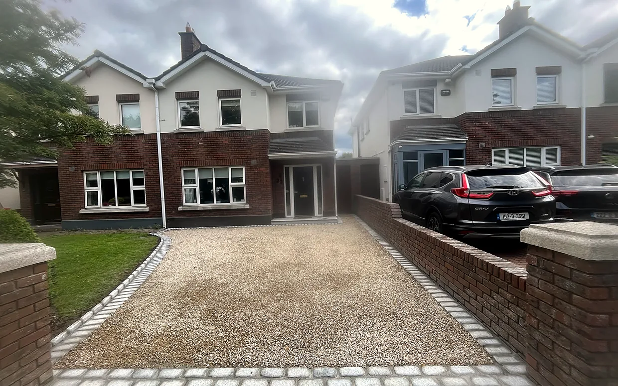 A gravel driveway with a silver granite cobble border and apron at a semi-detached house, with the lawn kept alongside.