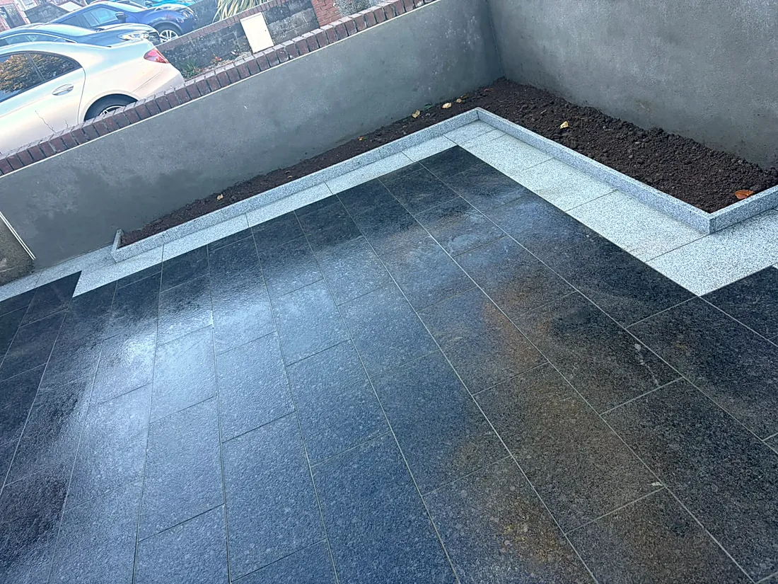The black granite driveway wet after rain, the silver granite border and the raised bed inside the gate