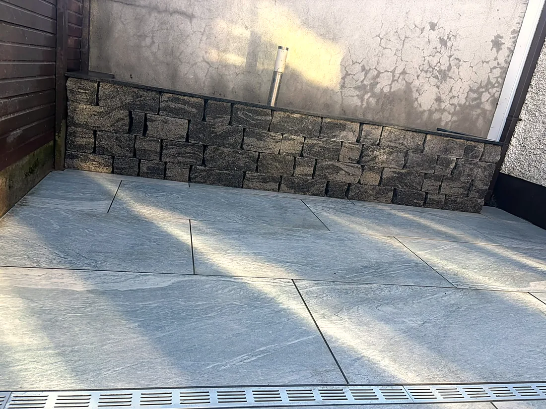 The porcelain patio at the stone-faced garden wall, a drainage channel along its foot
