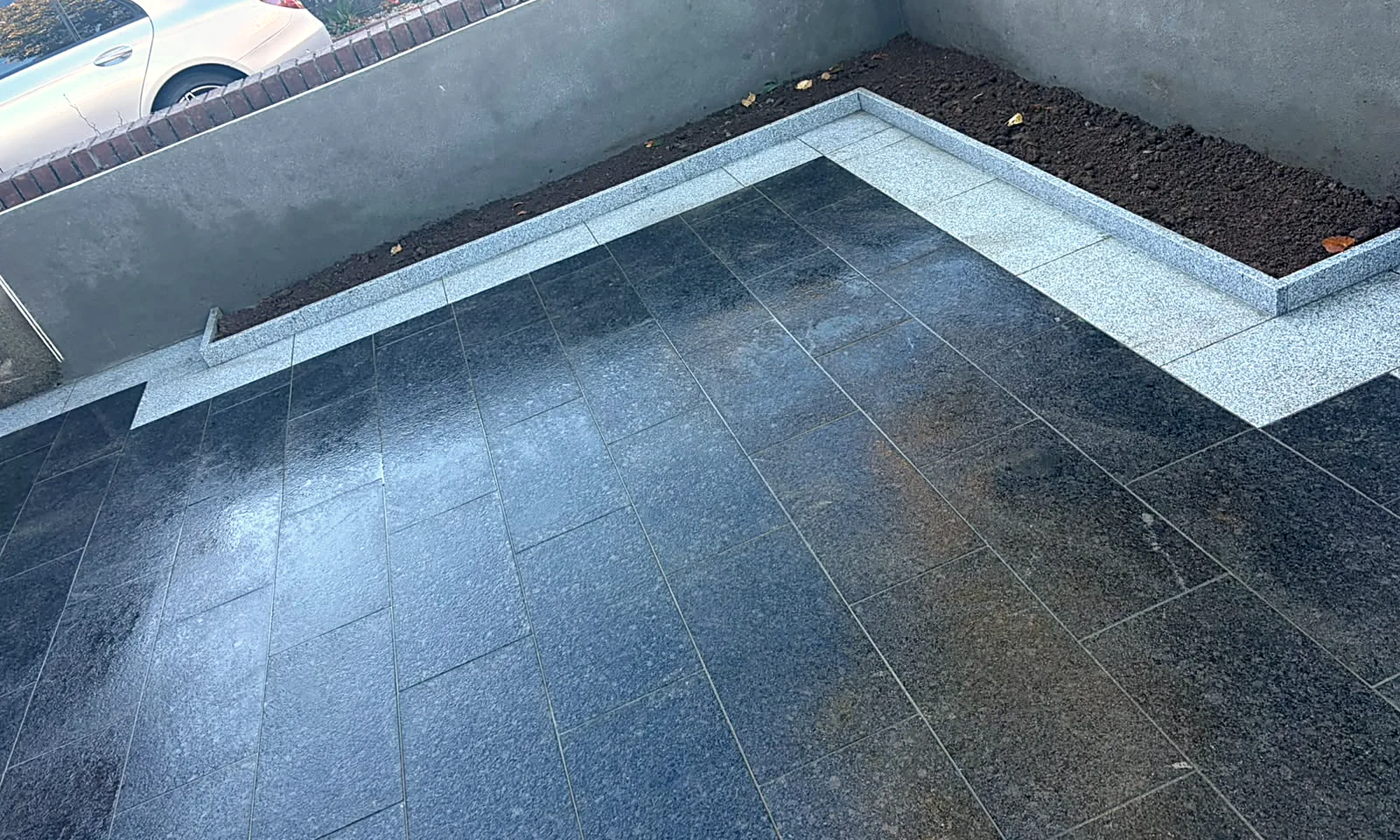 The black granite driveway wet after rain, the silver granite border and the raised bed inside the gate