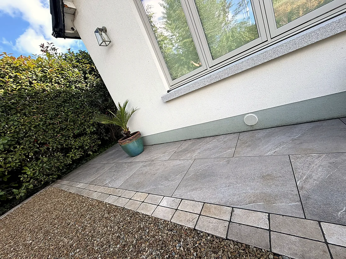 Porcelain paving along the front of the house in Foxrock, the gravel drive meeting it at a limestone cobble edge