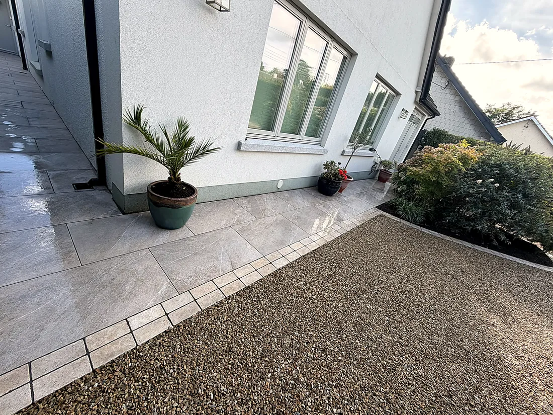 The porcelain path along the house wall, plant pots at the window, gravel beyond the cobble edge