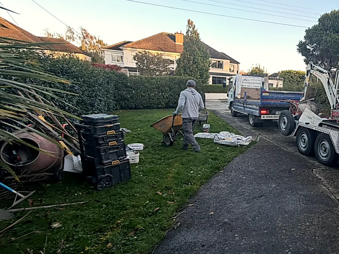 Mid-work: a worker with a wheelbarrow on the lawn beside the mixer, the old drive still in